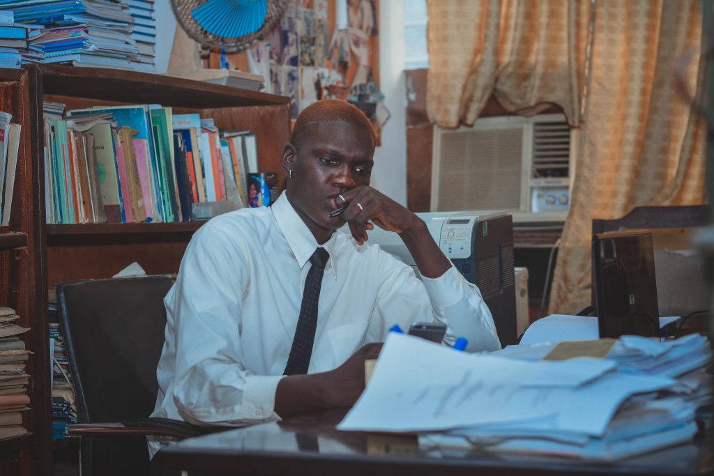 A focused adult man working at a cluttered office desk surrounded by books.